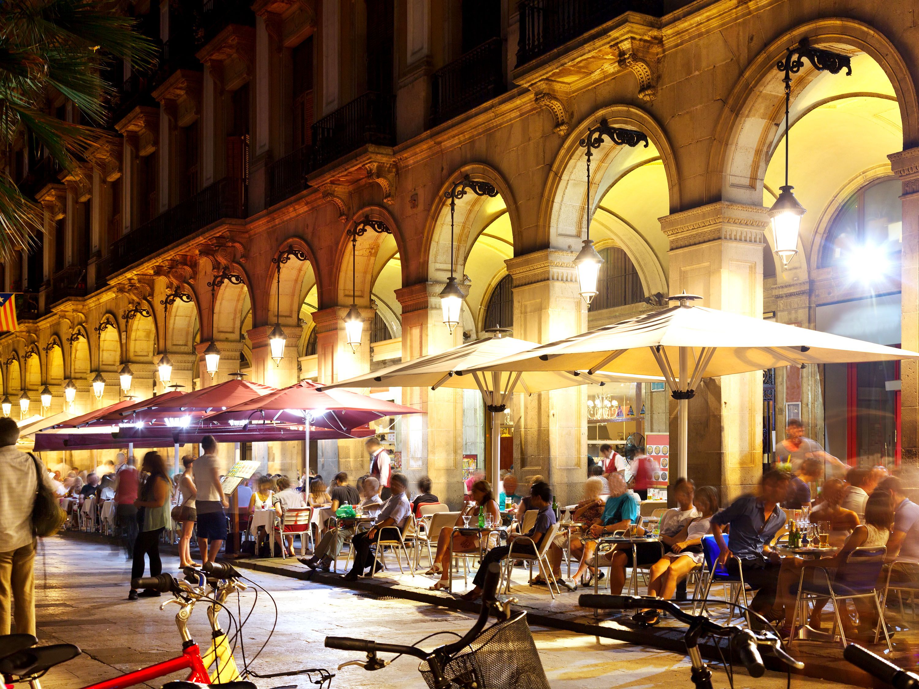 People sit in a crowded outdoor café at tables with umbrellas.