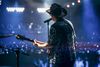 Perspectice from behind on stage of a musician with guitar and cowboy hat performing for crowd.