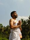 A bearded yoga teacher wearing a white robe, his hands in prayer, in Mysuru, India