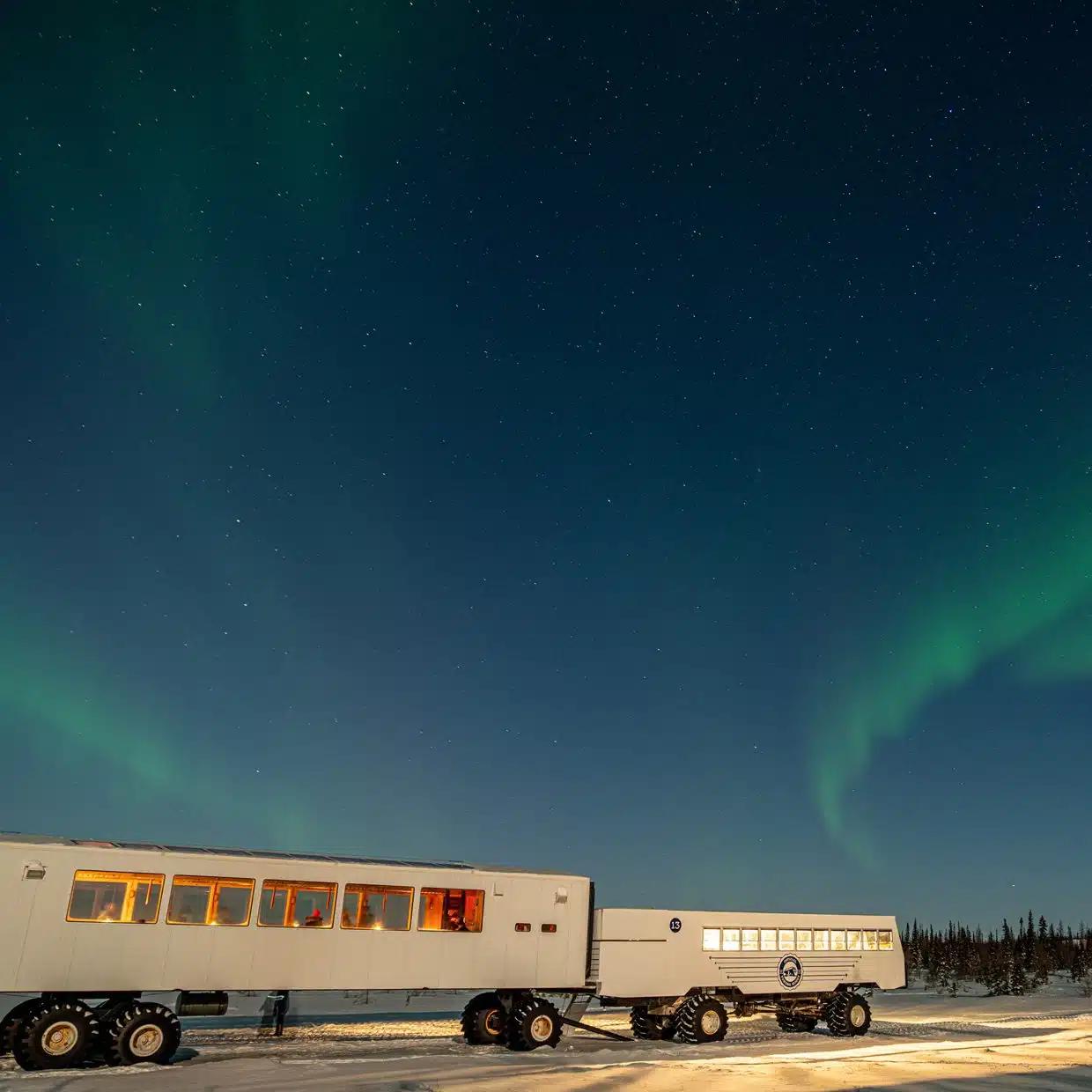 The northern lights seen above Dan’s Diner, Manitoba, Canada, two carriages on wheels with warm light glowing inside
