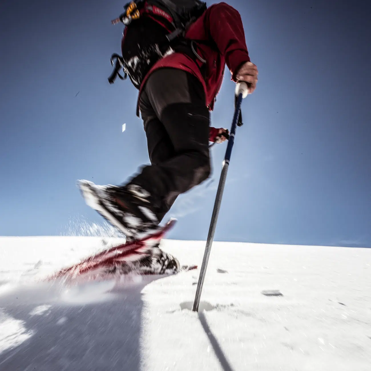 A close up of a person snowshoeing up a snowy hill in bright sunshine