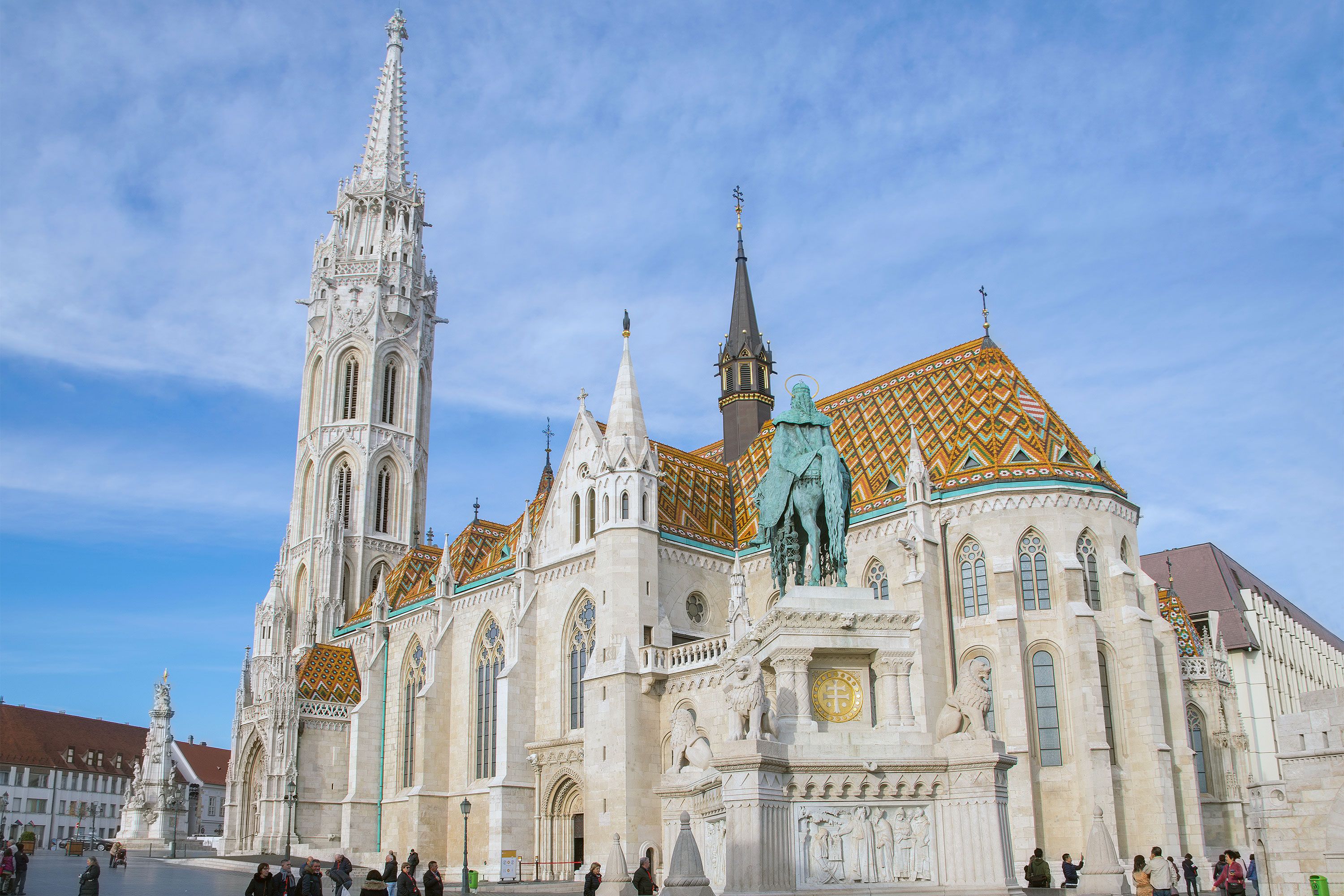 An exterior view of Matthias Church in Budapest showcasing the church’s Gothic spires, detailed façade, and distinctive multicolored glazed-tile roof under a bright sky.
