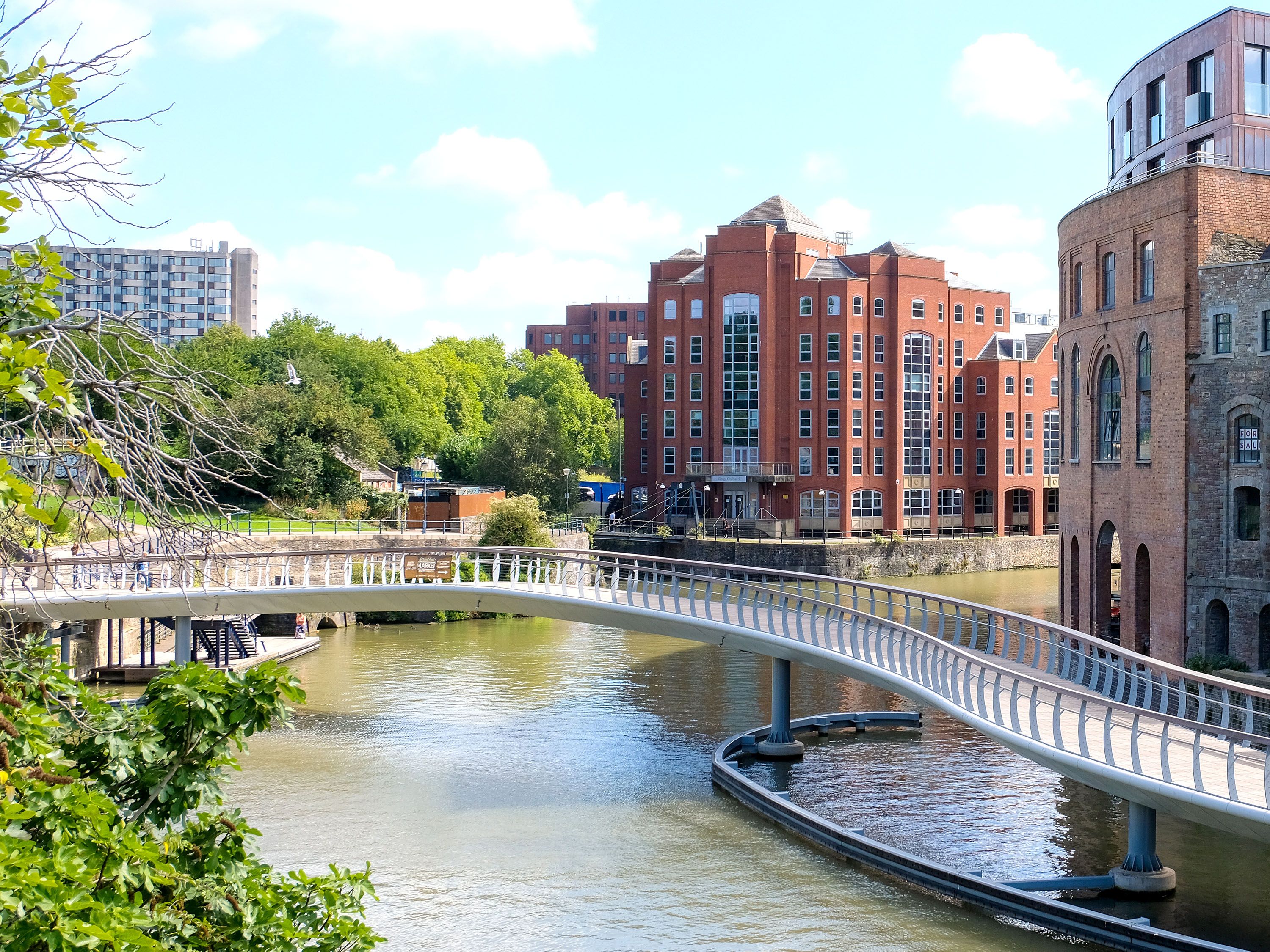 River with pedestrian bridge and brick buildings.