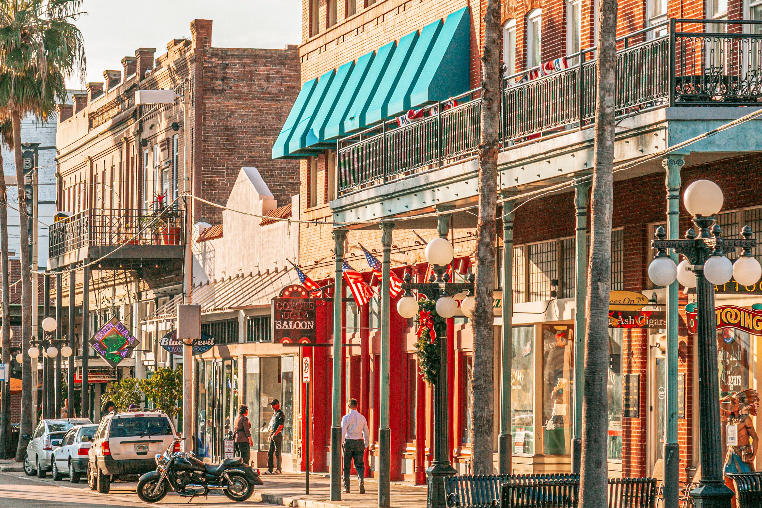 Street scene in Little Havana in Miami with pedestrians on a sidewalk and parked cars and a motorcycle on a sunny afternoon.