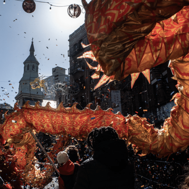 A Chinese dragon moving along the streets of New York, with paper lanterns seen behind, as part of Lunar New Year celebrations