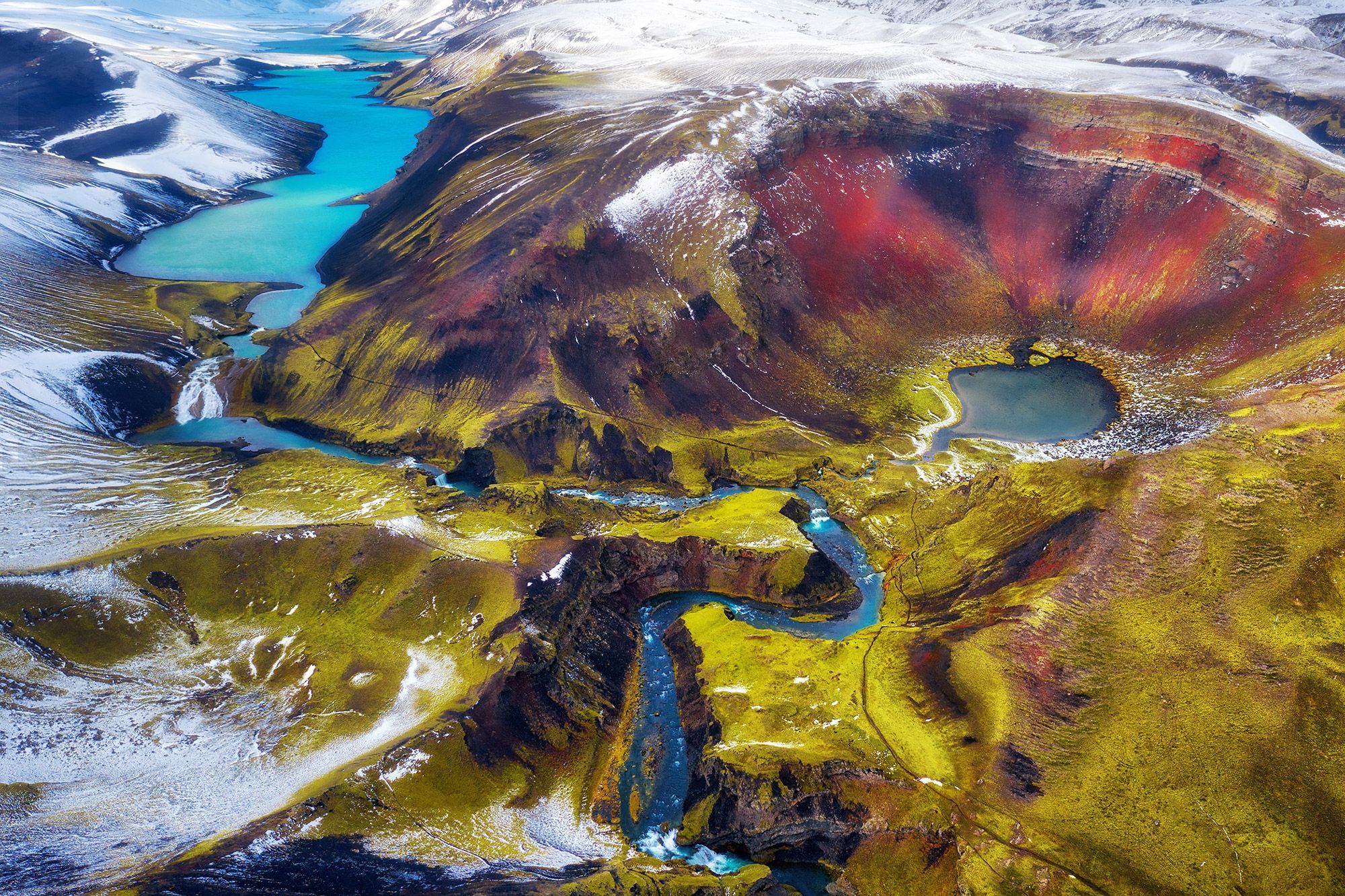 A volcanic crater with shades of red and green and a turquoise water running through in the Highlands in Iceland.