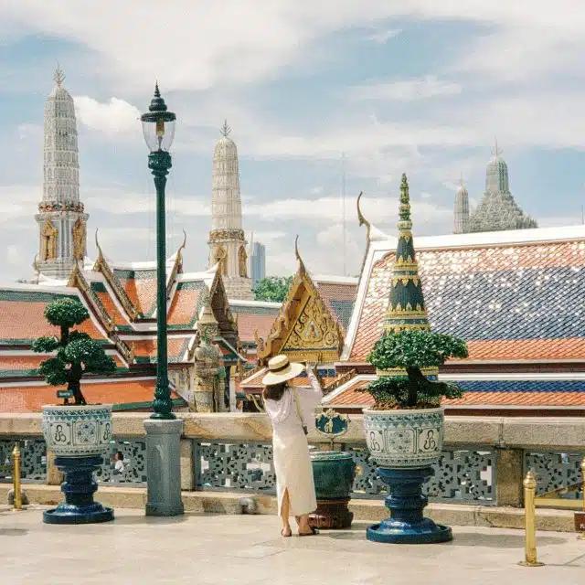 Beneath a blue sky with fluffy white clouds, the roofs of the Grand Palace Bangkok in Thailand glitter in the sunlight
