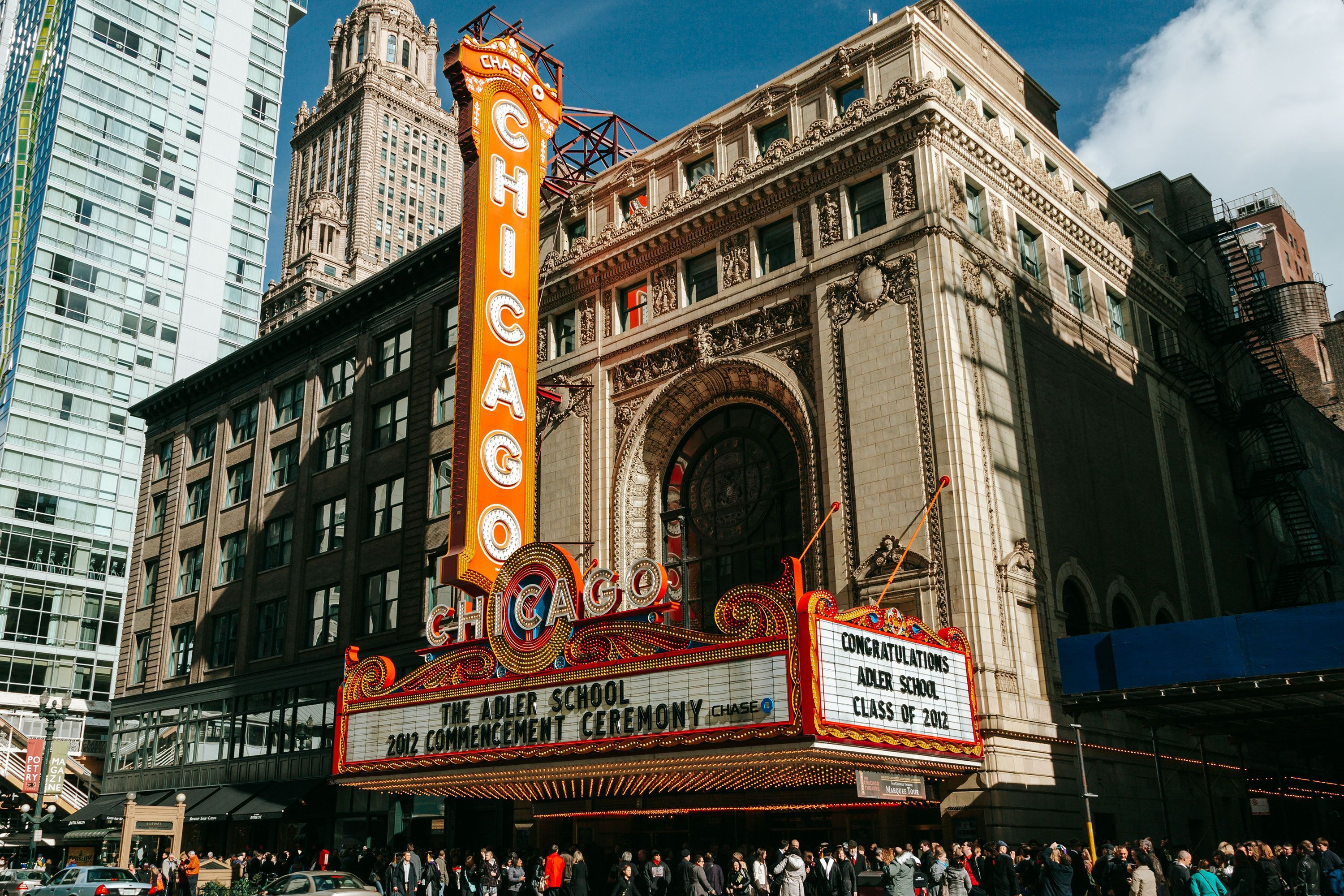 An exterior view of the Chicago Theatre featuring its famous red vertical “Chicago” sign and illuminated marquee on a busy street in downtown Chicago.