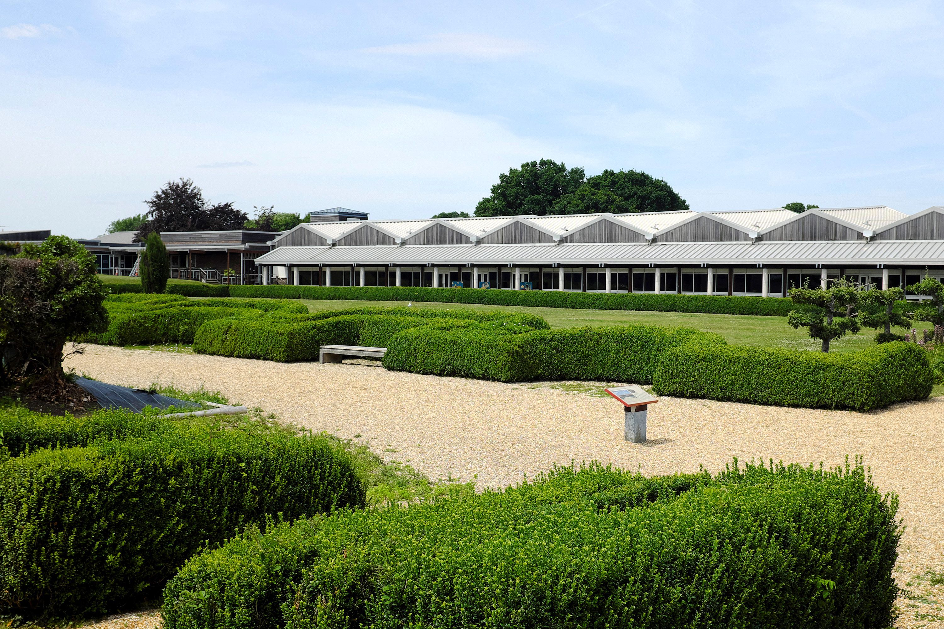 Hedges line a walkway and a short, long building in the background.