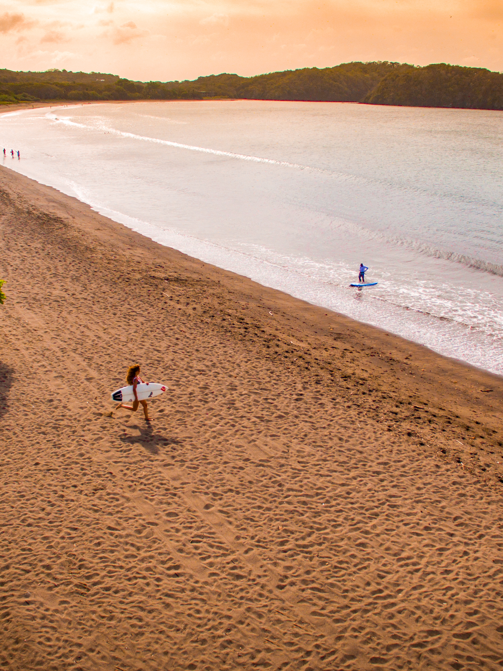 A person with a surfboard runs across a golden beach into the ocean