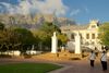 View of the Iziko South African Museum entrance and surrounding trees with people walking in the foreground and Table Mountain towering behind.