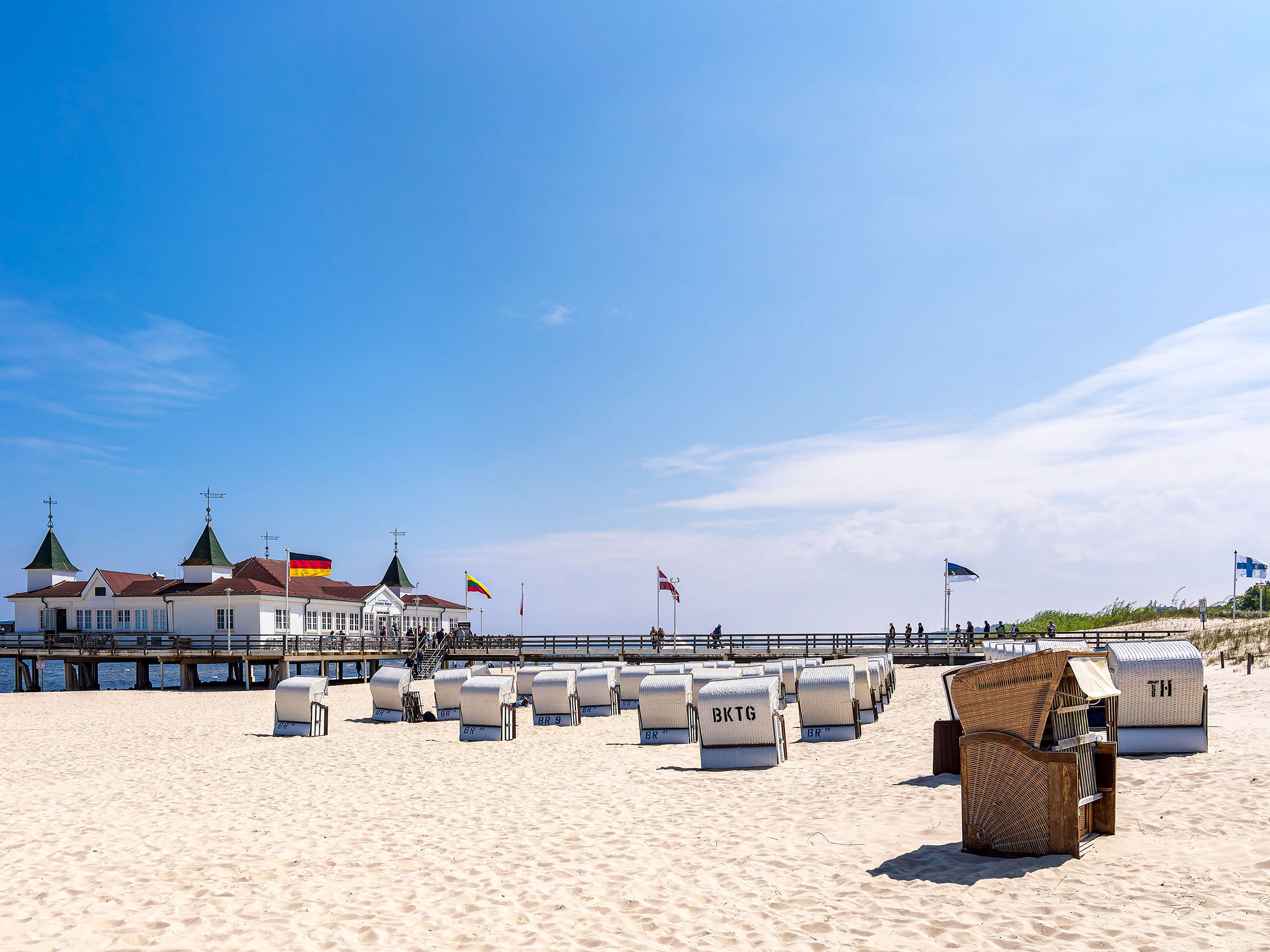 Beach chairs on white sand beach with pier in the background.
