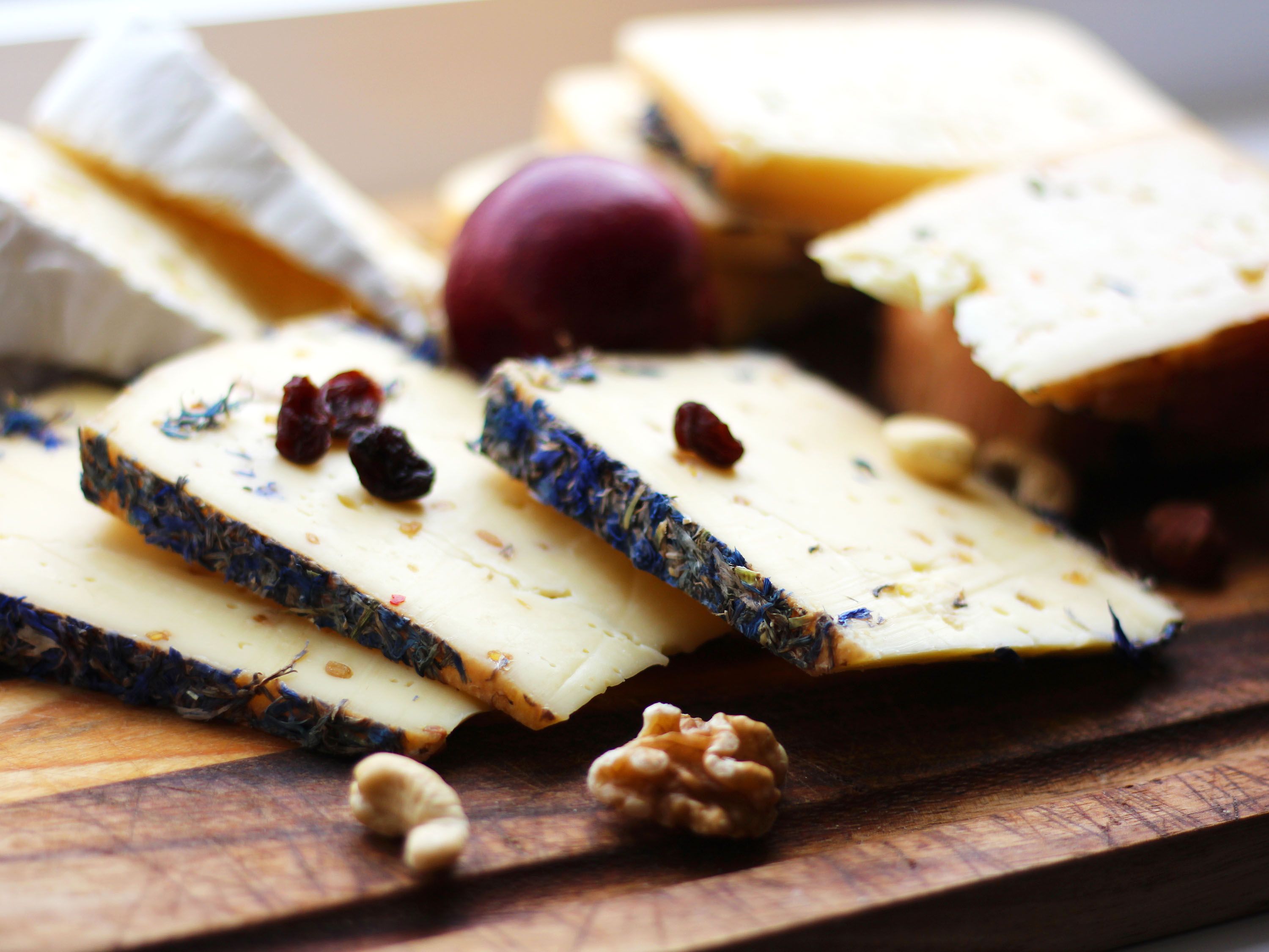 Three thin slices of cheese and nuts on a wooden board.