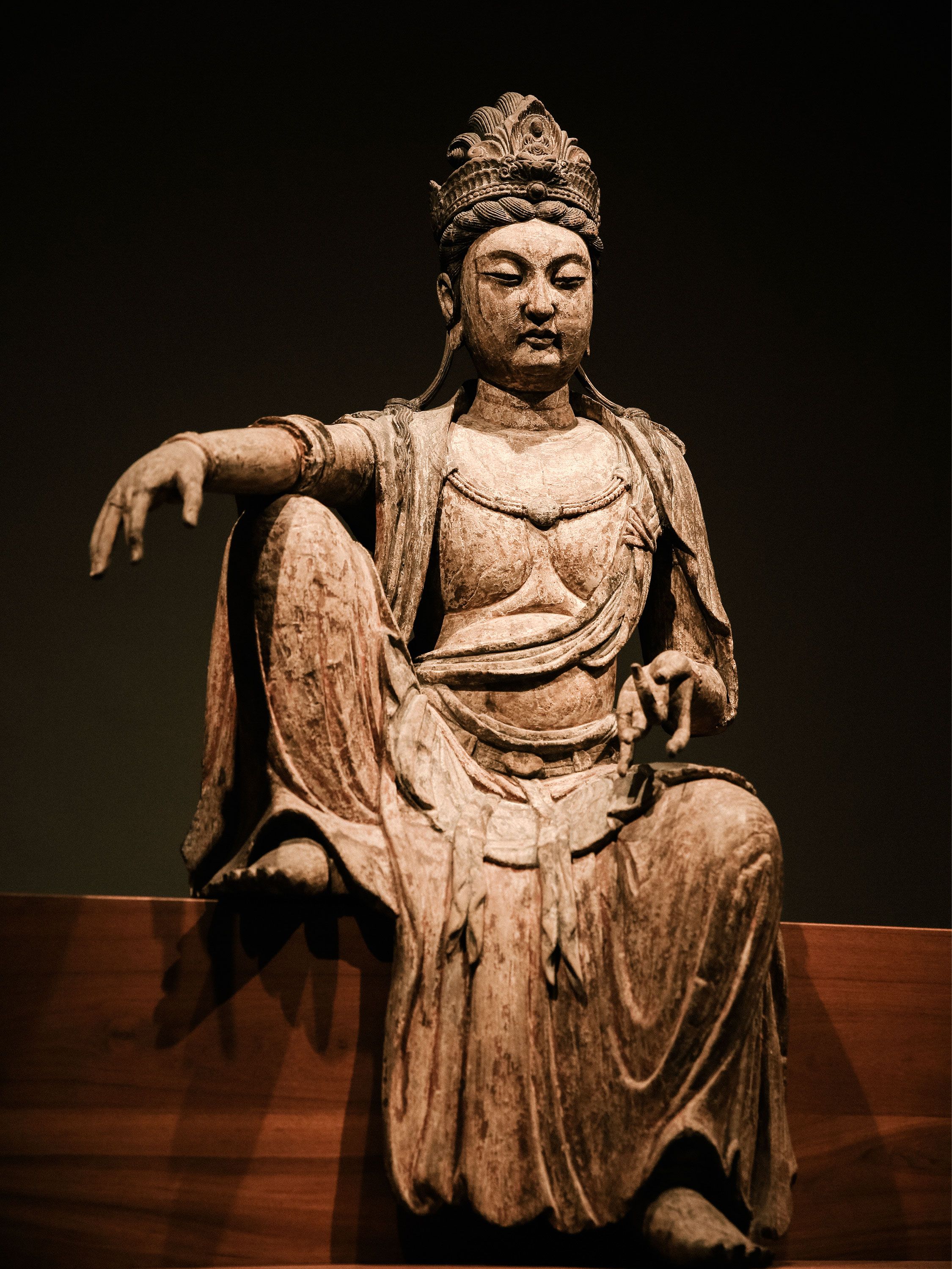 A seated wooden Buddhist statue displayed against a dark museum wall.