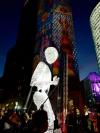 An illuminated puppet of an android, several times taller than a human, is walked through the streets of Berlin during the Festival of Lights