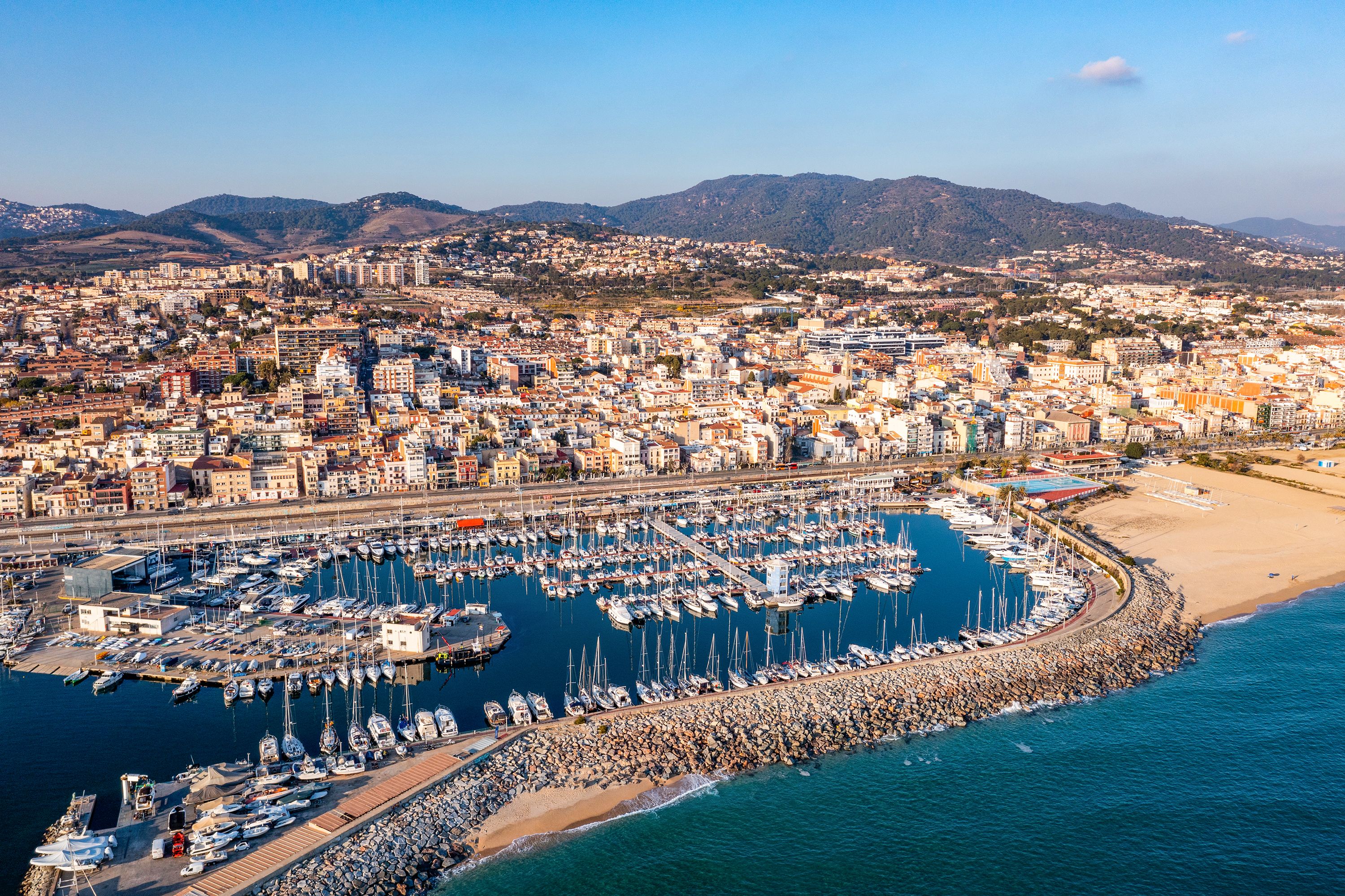 Overhead view of port and beach with town with buildings and hills in the background.