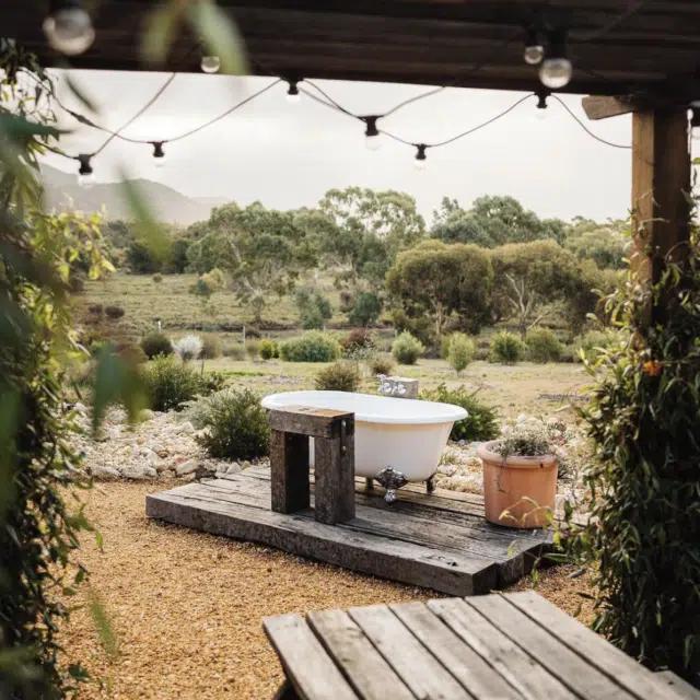 An outdoor bathtub on decking in the back yard of the Nook on the Hill cabin in Victoria, Australia, with countryside view beyond