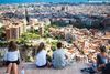 A group of people sitting on top of the Bunker del Carmel looking out over a view of the city of Barcelona.