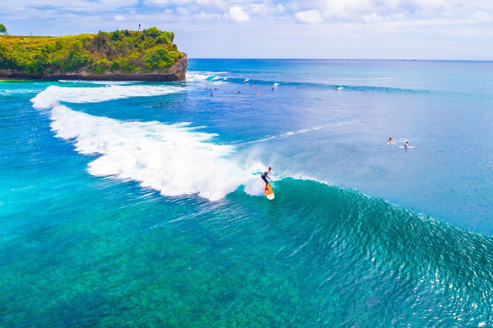 Surfer riding a turquoise wave off Bali’s tropical coastline.