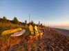 Kayaks and adirondak chairs on the beach as the sun sets.