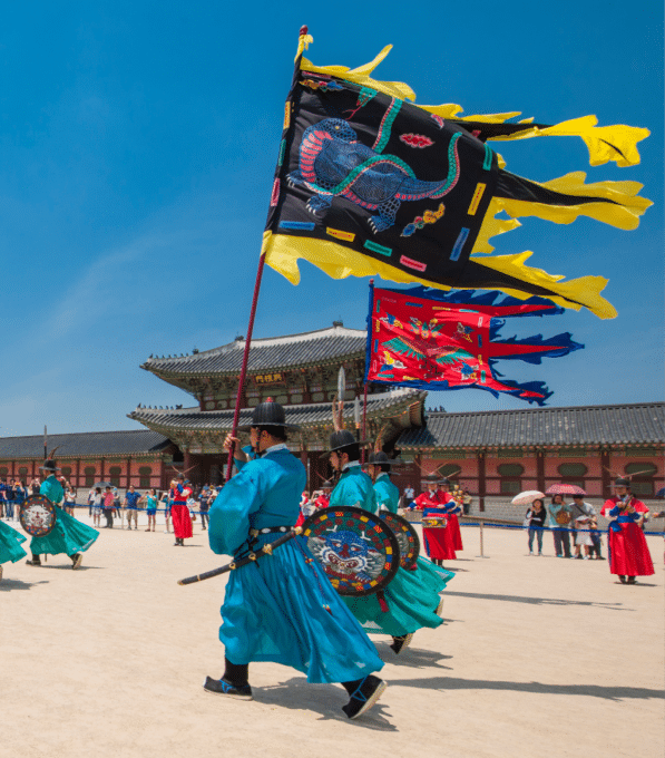Palace guards at Gyeongbokgung Palace in Seoul parade in bright blue and turquoise robes, carrying colorful shields and flags