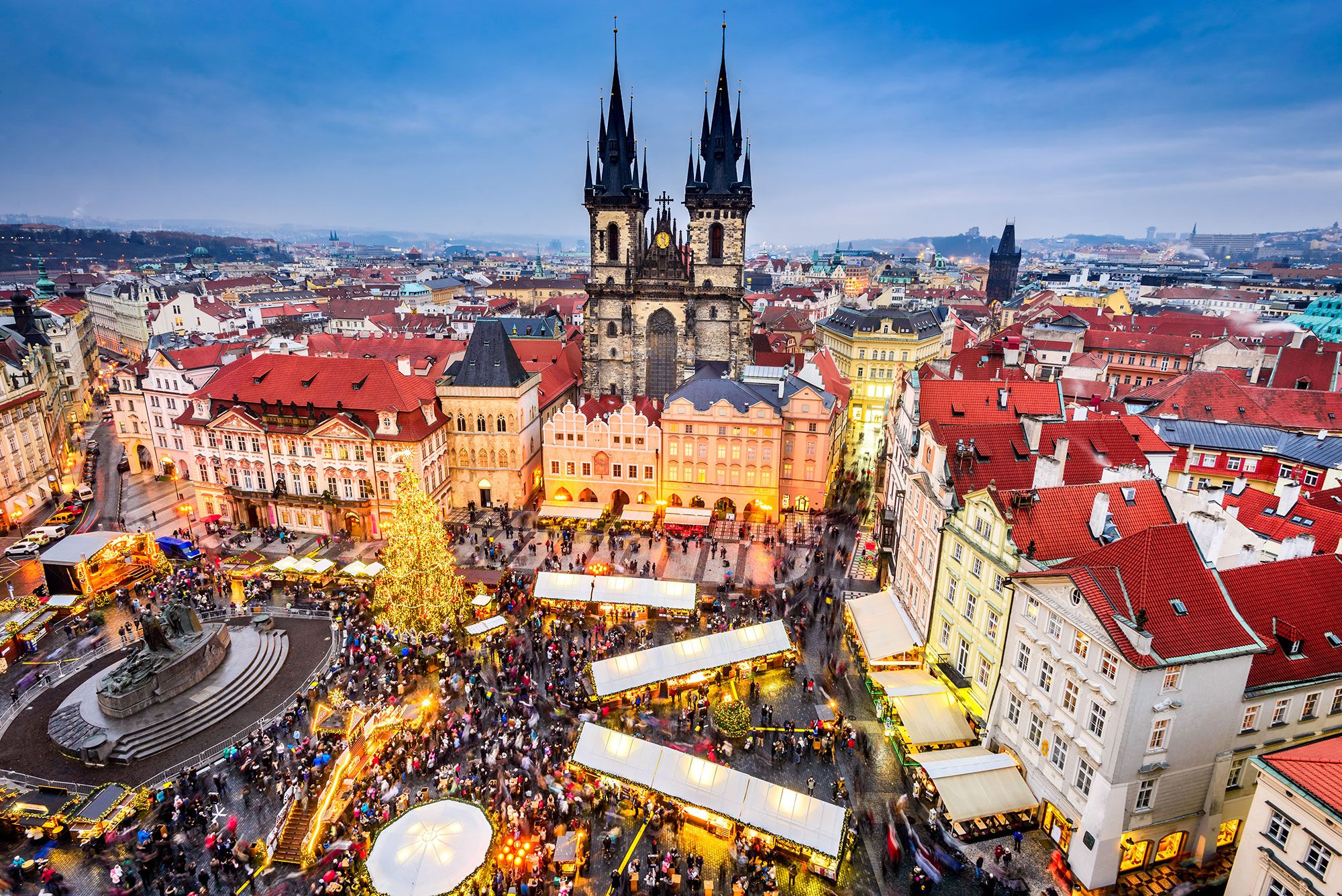 Aerial view of a square in a European city lit up during Christmas time with a church building standing tall in the distance.
