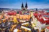 Aerial view of a square in a European city lit up during Christmas time with a church building standing tall in the distance.
