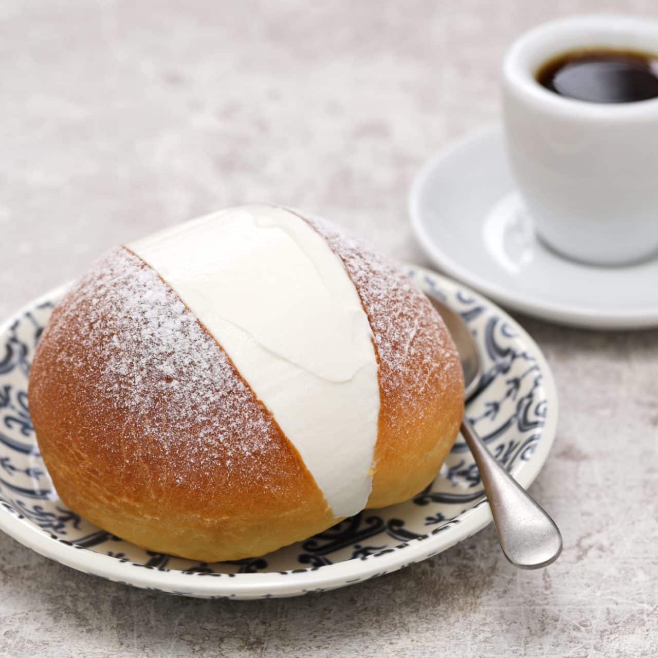 A maritozzo, or cream-filled roll, on a pretty patterned plate, with a double espresso
