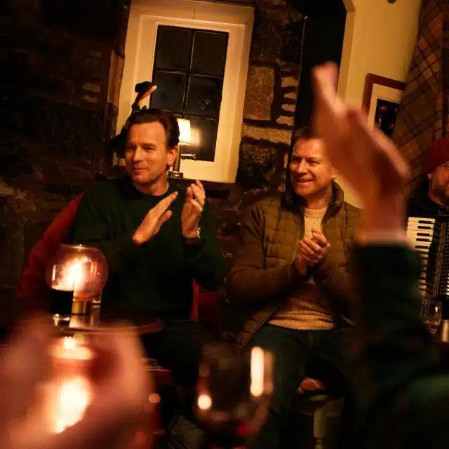 Ewan McGregor and his brother Colin McGregor clap along to the music in the Fortingall Hotel and Ewe Bar, Scotland