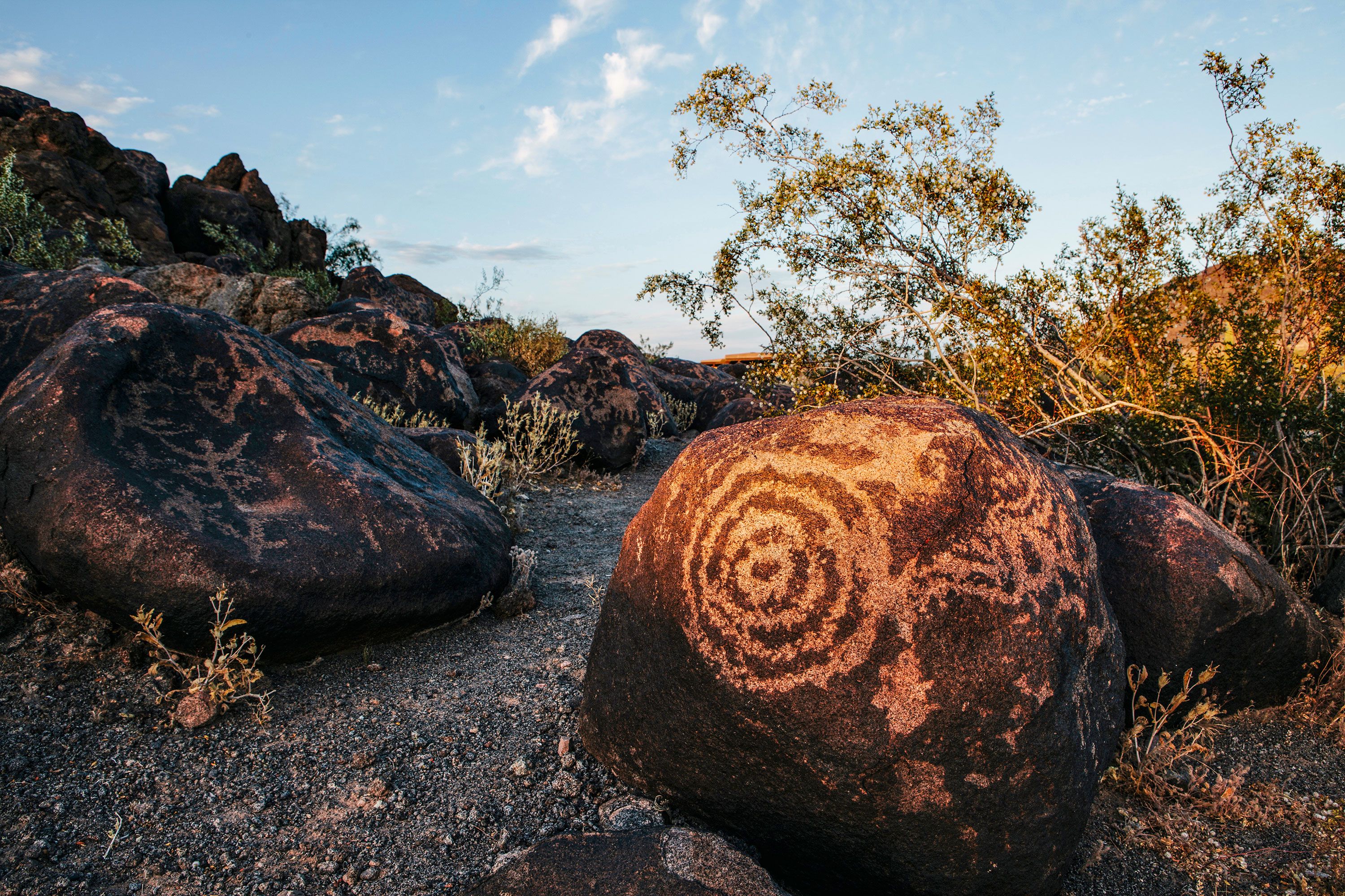 Primitive rock art along a dirt and stone path at sunset.
