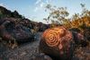 Primitive rock art along a dirt and stone path at sunset.