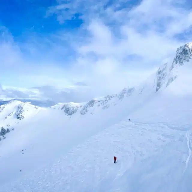 People ski along the side of a snow-covered mountain beneath blue skies