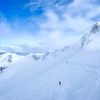 People ski along the side of a snow-covered mountain beneath blue skies