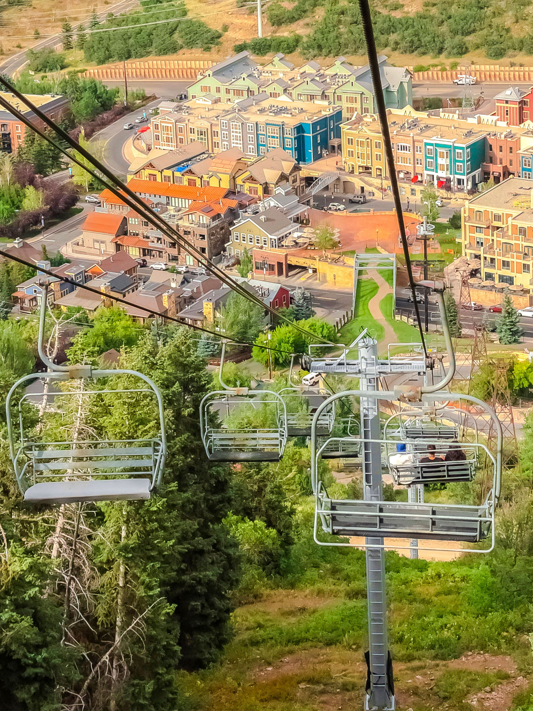 Chairlifts glide over trees toward a colorful mountain resort village.
