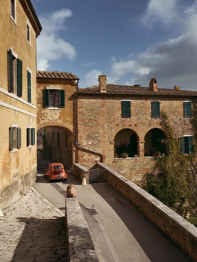 A red Fiat 500 drives through a stone archway in the tiny medieval hamlet of Lucignano d’Asso, Italy