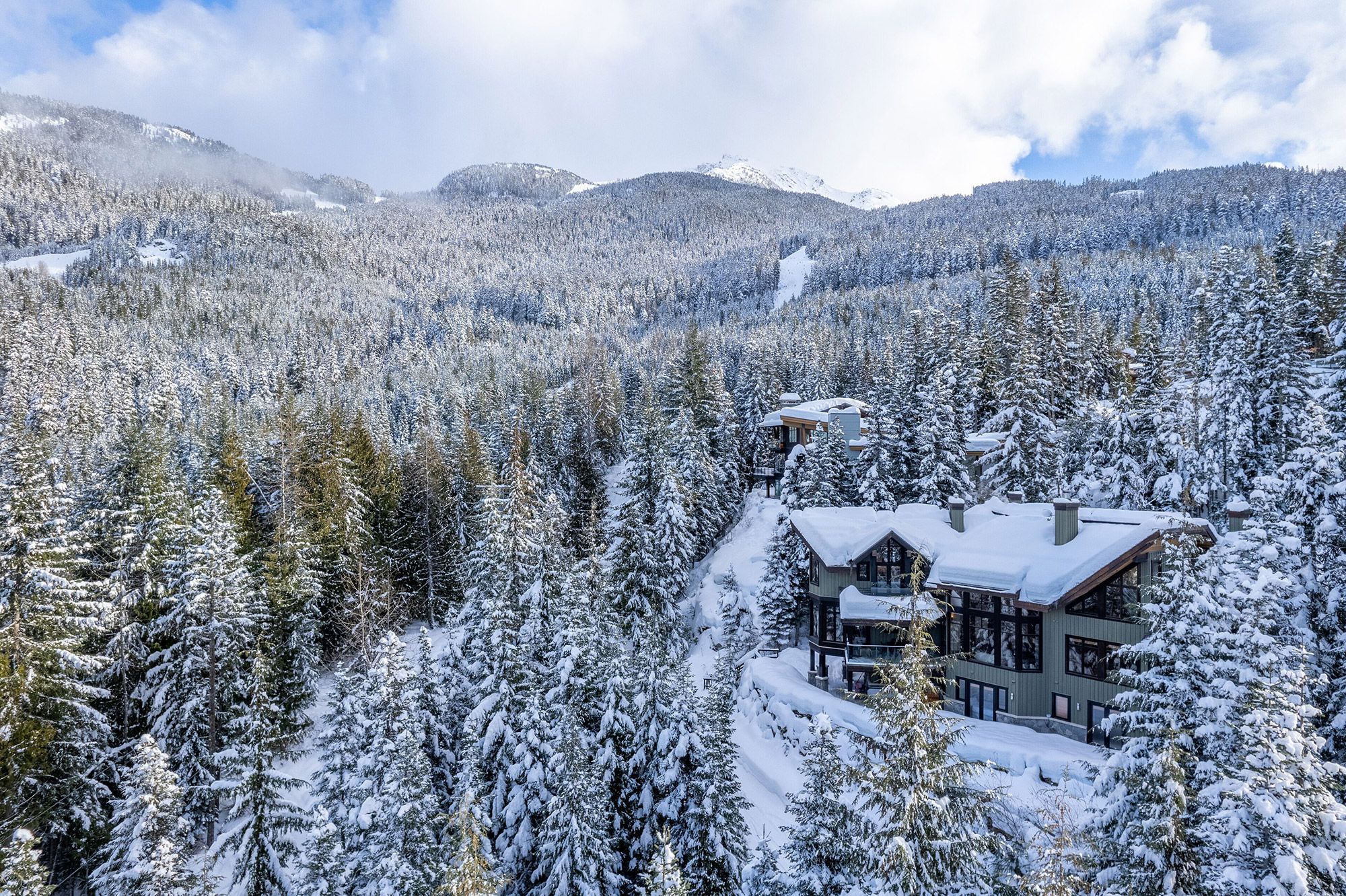 Ein Ferienhaus im alpenländischen Stil in einer verschneiten Winterlandschaft, im Hintergrund die verschneiten Berge