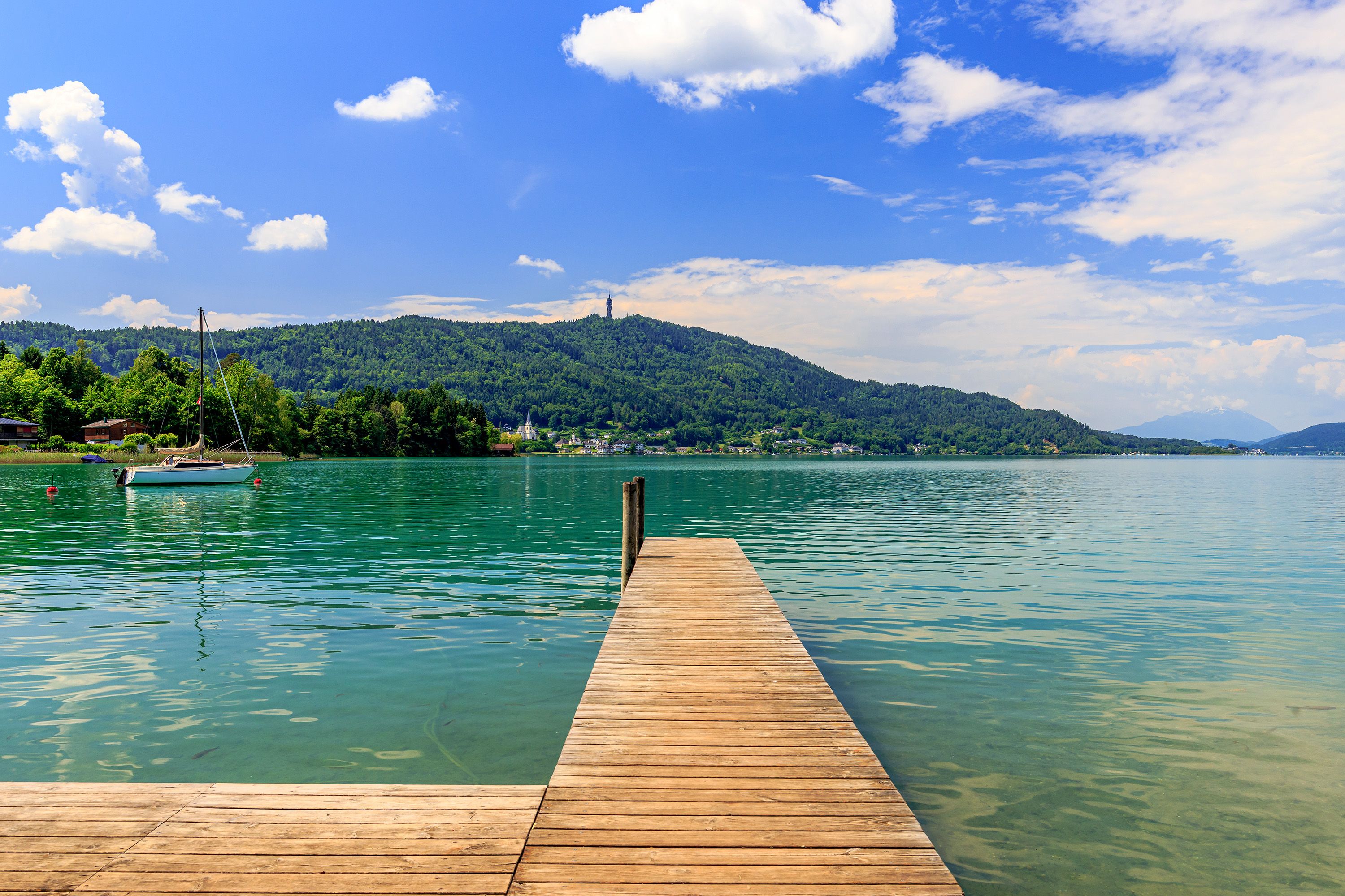 A wooden pier reaches into the water where a sailboat is moored.