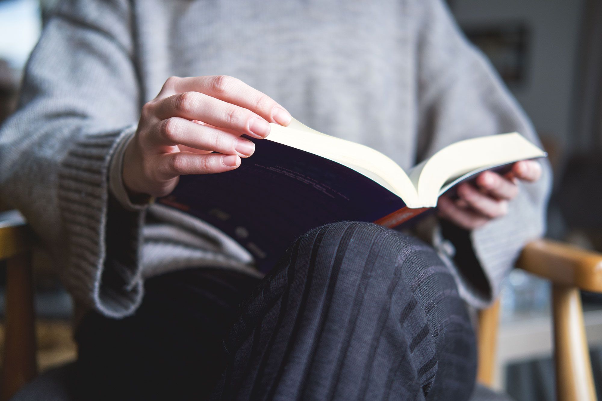 Woman sitting with crossed legs holding an open book in her lap.