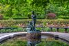 Bronze statue of two children playing instruments at the center of a small reflecting pool, surrounded by colorful tulips and lush greenery in Central Park’s Conservatory Garden.