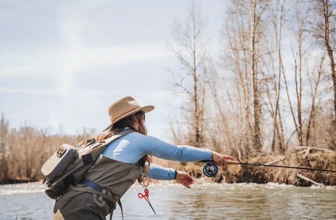 Wearing a hat and waders, Lindsay Kocka casts a line into a river