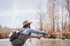 Wearing a hat and waders, Lindsay Kocka casts a line into a river