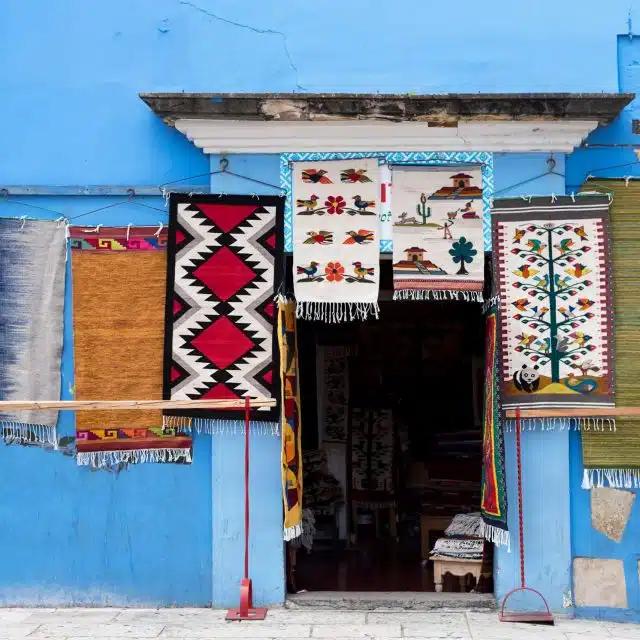 Brightly colored textiles hang outside a sky-blue building in Oaxaca, Mexico