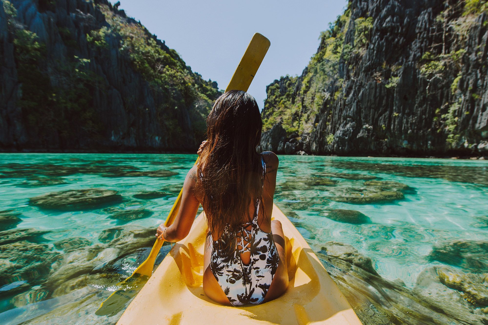 A woman on the front of a boat paddling through a lagoon with cliffs on either side of her in the Philippines.