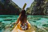 A woman on the front of a boat paddling through a lagoon with cliffs on either side of her in the Philippines.