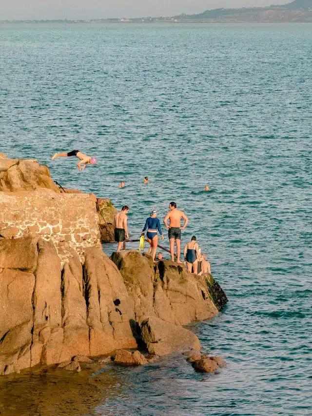 People stand on the rocky coastline ready to go wild swimming at the Forty Foot in Dublin, Ireland