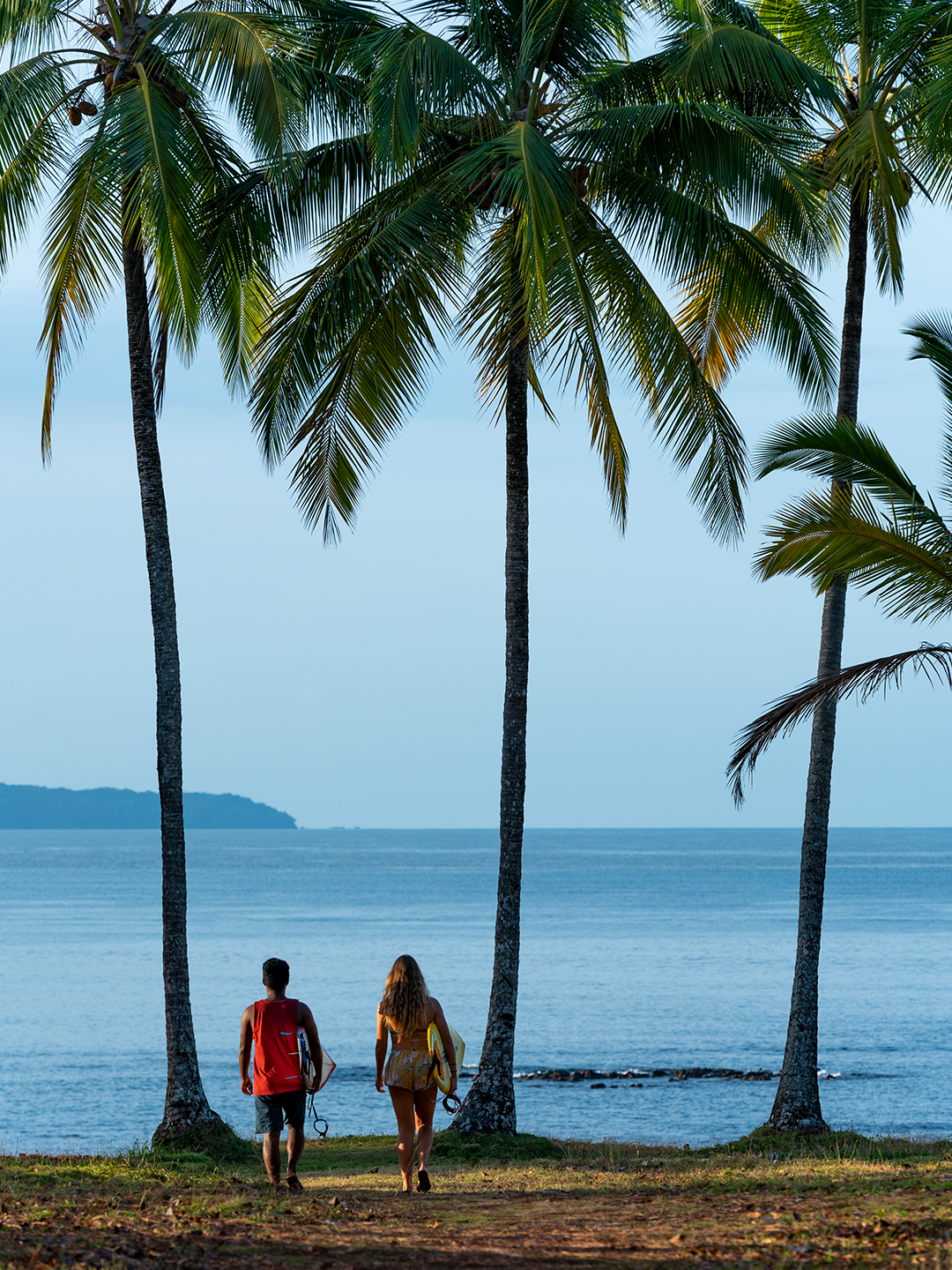 Two people walk under palm trees overlooking the blue ocean in Santa Catalina in Panama