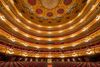 Gilded opera house interior with tiered balconies, chandeliers, and red seats viewed from the stage.