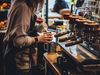 A woman barista pouring milk into a coffee cup next to a large espresso machine.