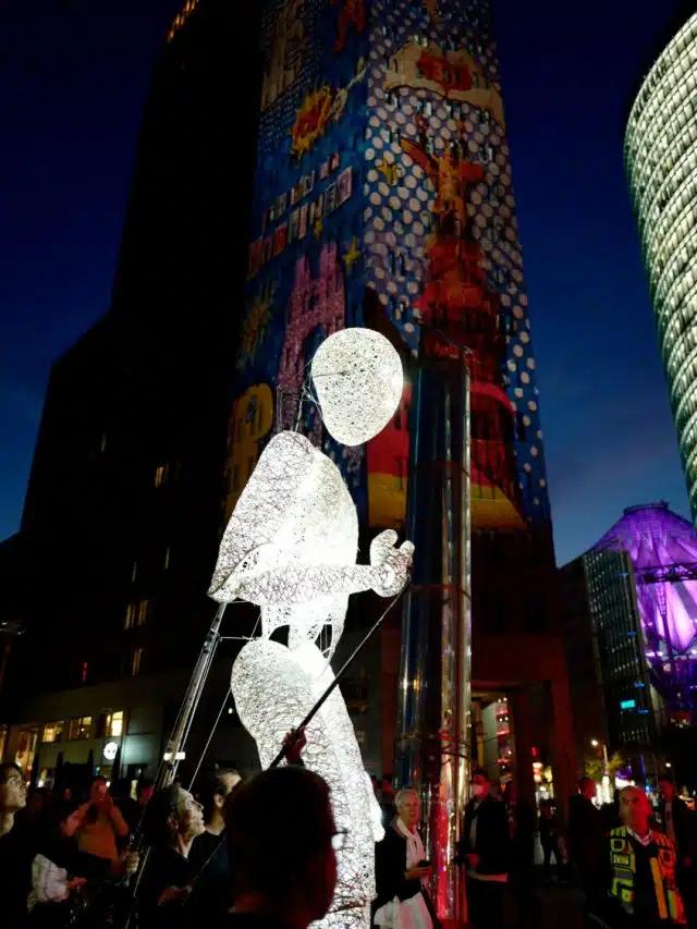 An illuminated puppet of an android, several times taller than a human, is walked through the streets of Berlin during the Festival of Lights