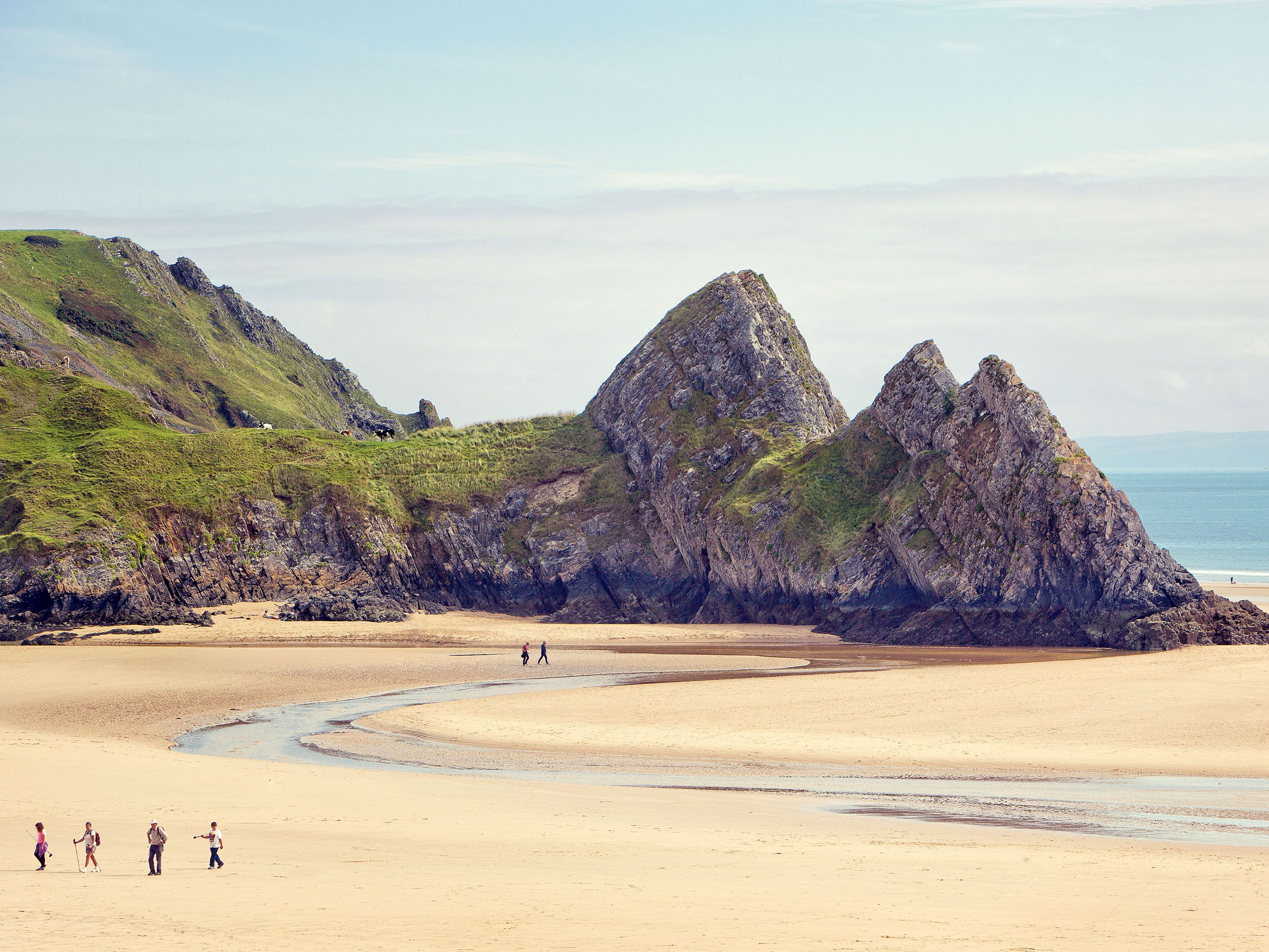 People walk on a white sand beach with large rock formations.